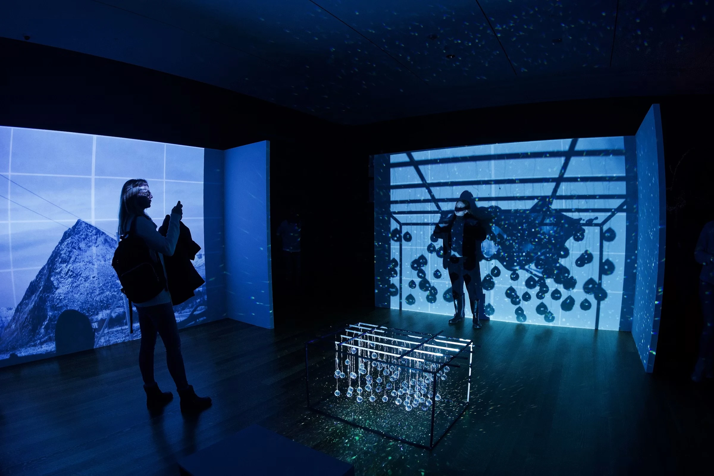 Visitors in an immersive projection room with wall-sized projections and a light installation